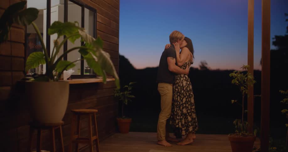 A man and woman dancing together on the porch of a house at night share a kiss
