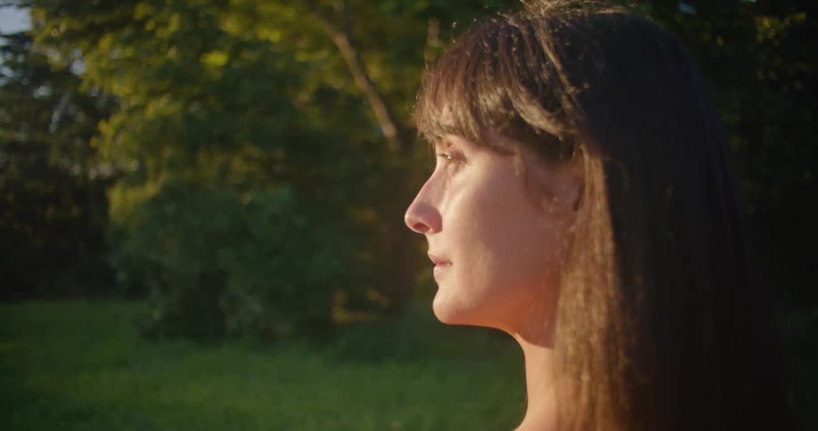 Close up of the face of a young woman standing on a fied at sunset