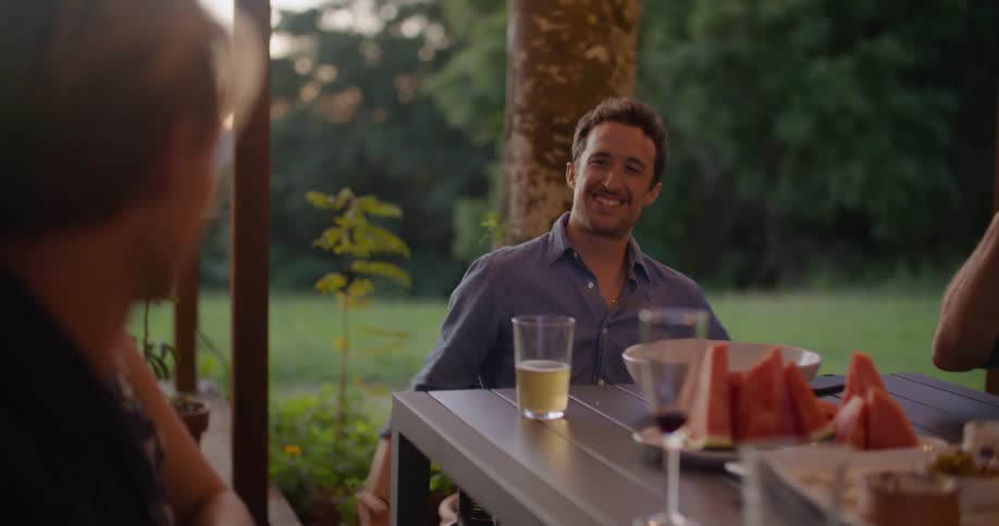 Group of friends laughing and talking on the table in the porch at home at sunset