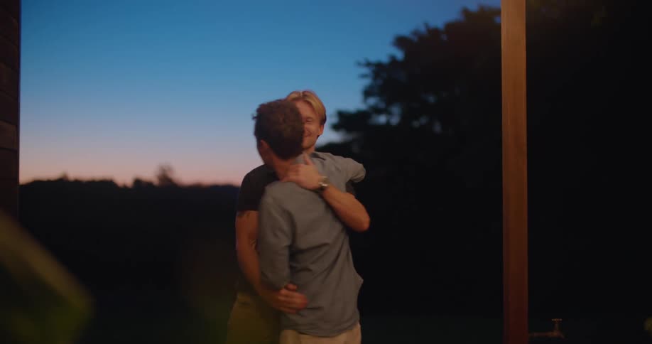 A man walking towards a house is greeted with a hug by another man before they continue towards the house together