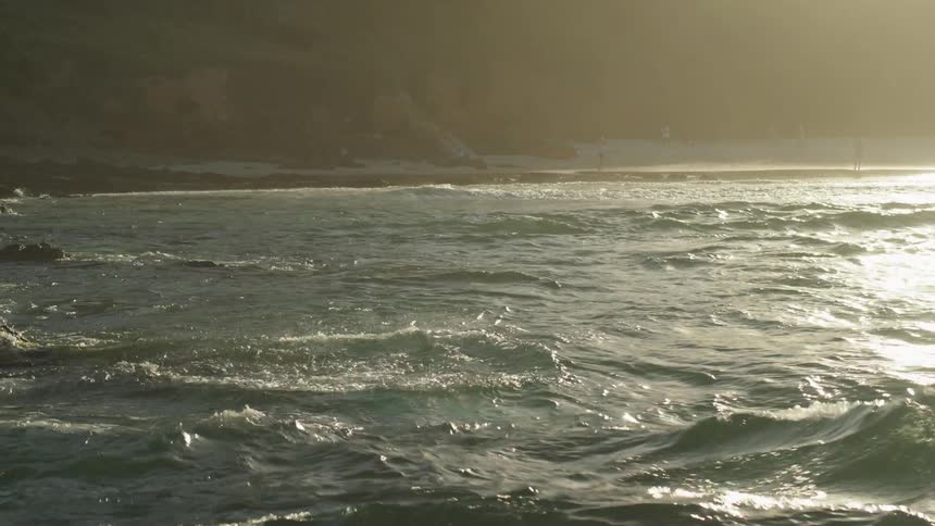 A man in swimming trunks dives off a rock and into the ocean