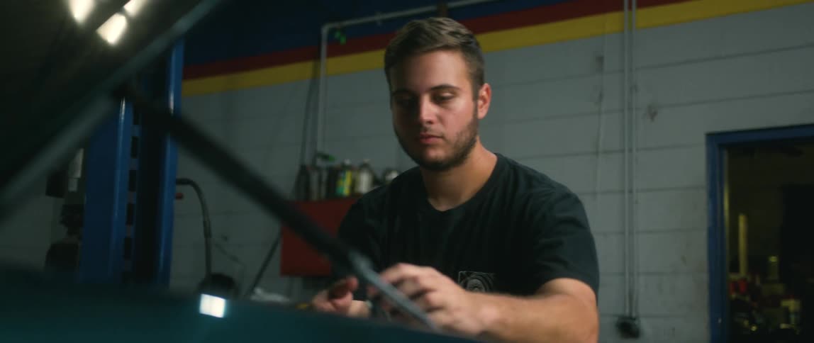 A man opens up the hood of a car and removes a cap and looks inside