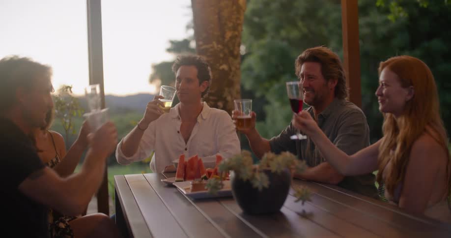 Group of friends toasting with wine on a dinner table on the porch at sunset