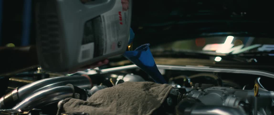 A person pours oil into a funnel in a car engine