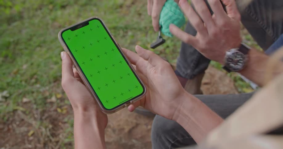 A woman holds a cell phone with a green screen with crosses on it as a man points at the screen and gestures with his hand