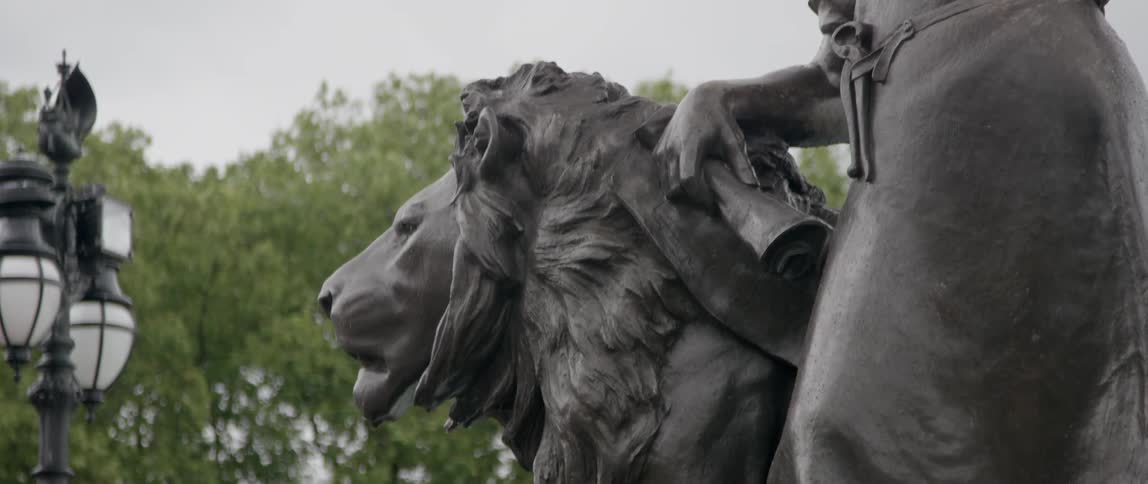 A lion's head on a bronze statue with trees in the background