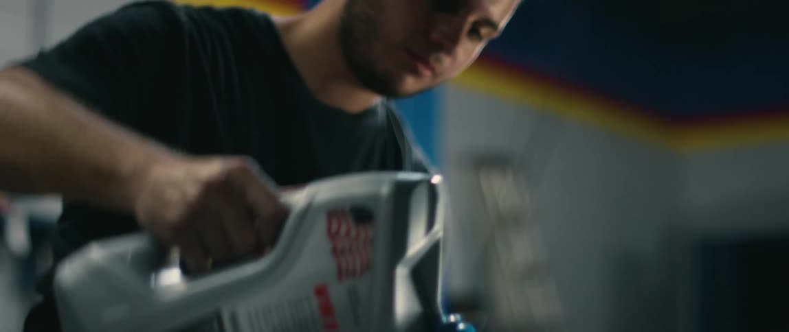 A man uses a funnel to pour oil into the engine of an automobile in a garage