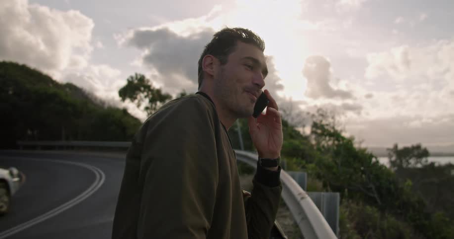 A man is on the side of a road talking on his cell phone