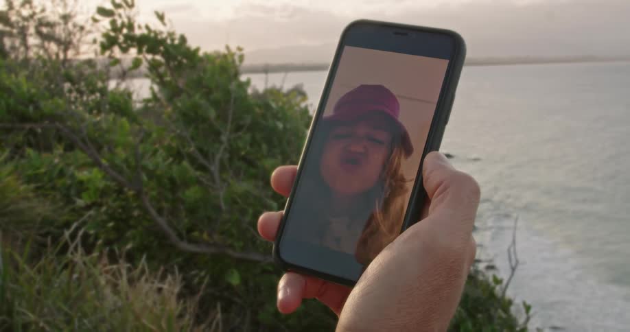 A little girl on screen talks with and makes a kissy face at dad who is holding the phone in his hand