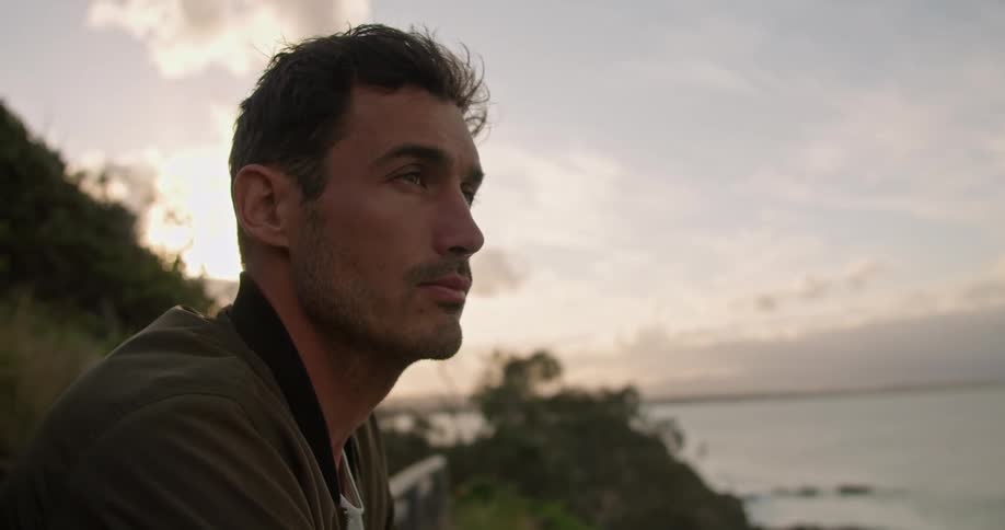 Man leans on surfboard sitting on rail as he looks across ocean