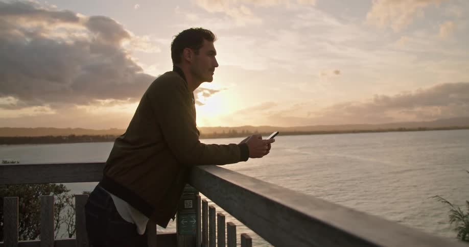A man is using his cell phone on the terrace facing the water
