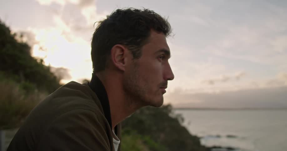 A man holding a surfboard watches the sunrise by the shore