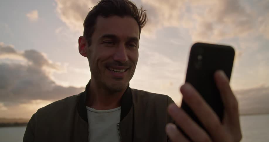 Young man talking on a phone near the ocean at sunset