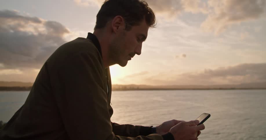 A man checks his cell phone as people surf below