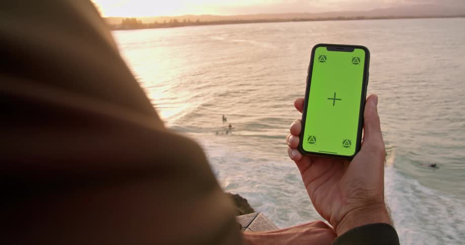 A man uses his smartphone while leaning on his balcony overlooking the coast