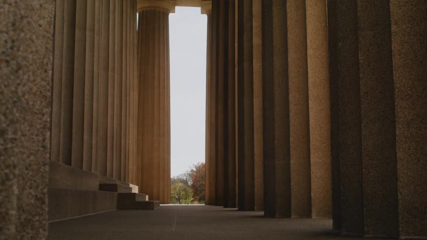Columns line path near stairs into building and lead toward sky and trees