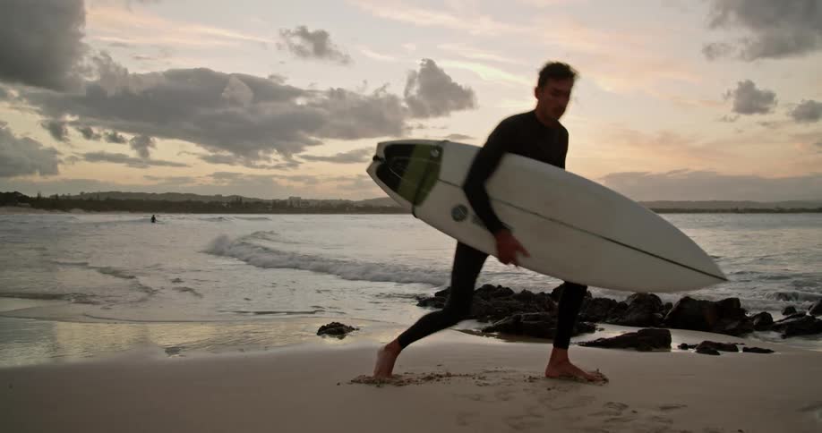 Surfer with wetsuit holds surfboard and warms up before surfing on the beach at dusk