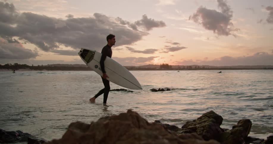 A man carries his surfboard under his arm as he wades in the ocean