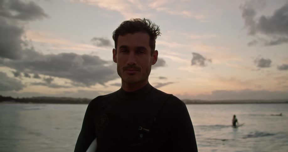 A man wearing a wetsuit and holding a surfboard is standing on a beach