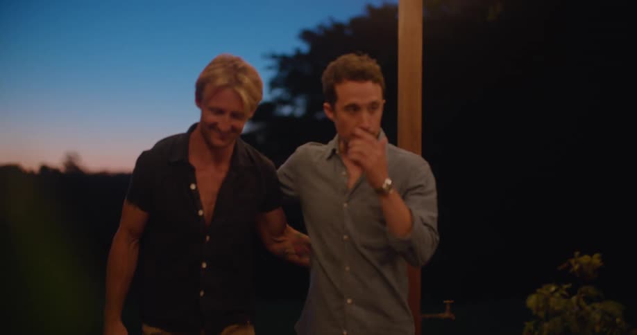 A man hugs and greets his friend as they walk onto a patio