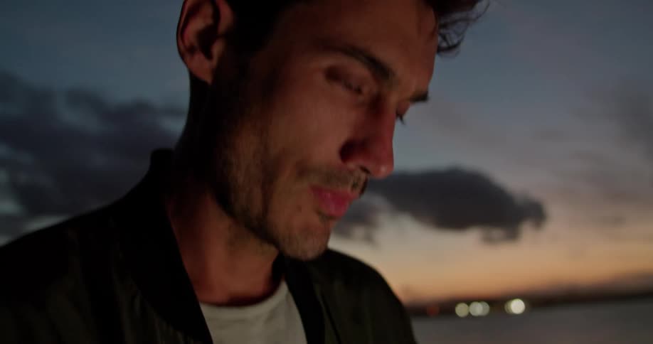 Man sits outdoors near water typing at night
