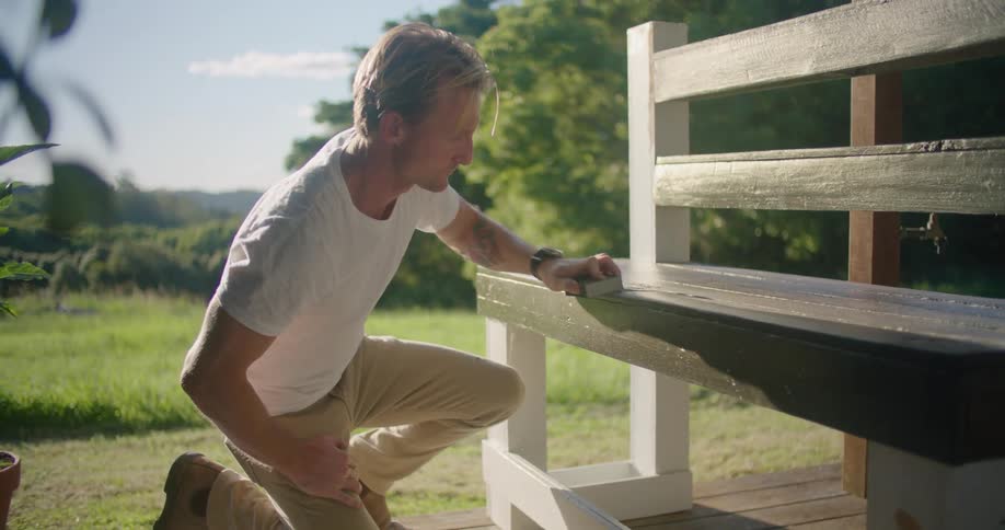 A man is sanding his wooden bench by hand