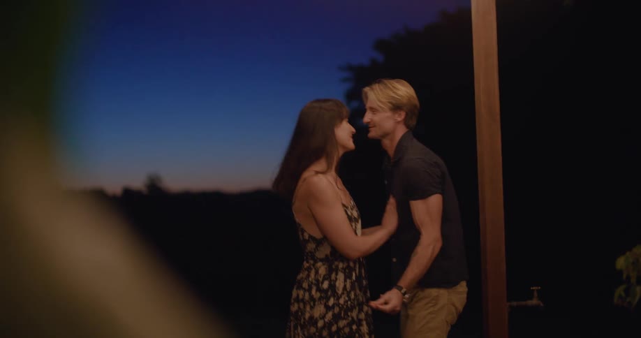 Couple dances barefoot together on wooden porch at night