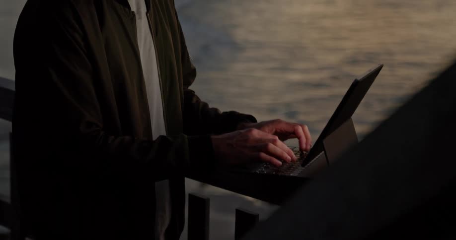 A man props his laptop on a balcony over the ocean