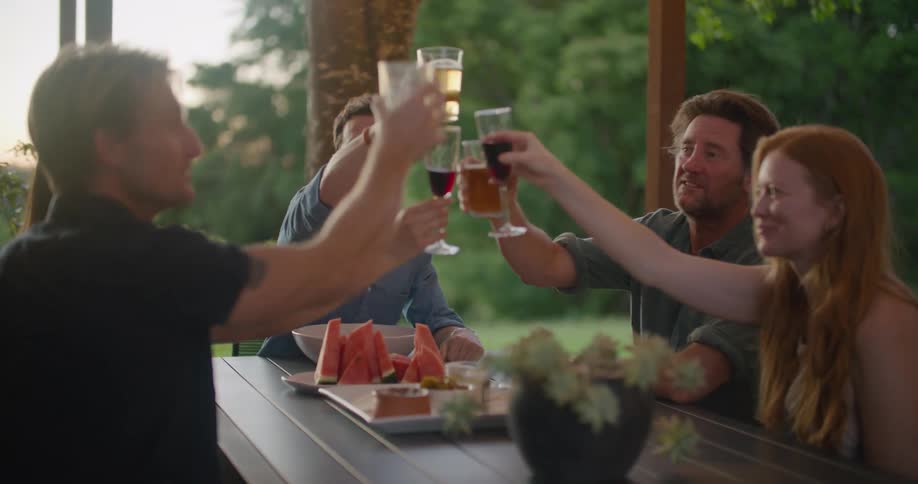 Group of friends talking and toasting with wine on a table in the porch at sunset