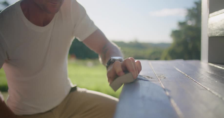 A man is sanding a wooden bench