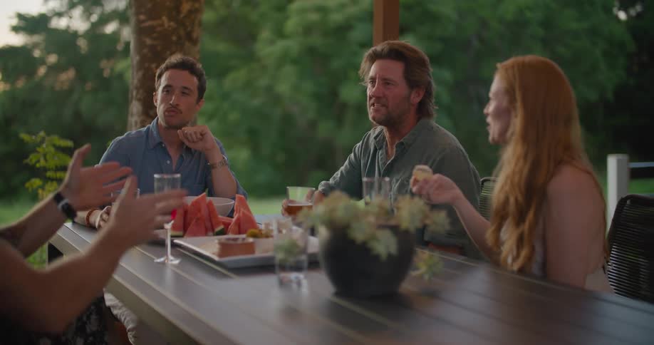 Group of happy friends eating food and talking on a table in the porch at sunset