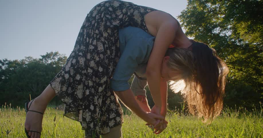 Man leans over holding woman on his back in field on sunny day