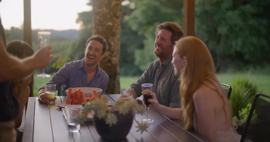 A man raises his wine glass to toast his friends as they eat outside