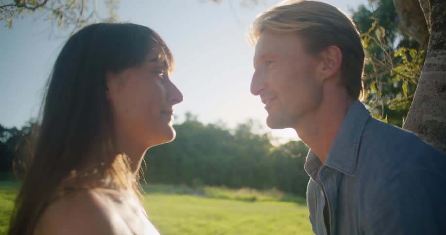 A woman leans in to kiss her husband as they lean against a tree