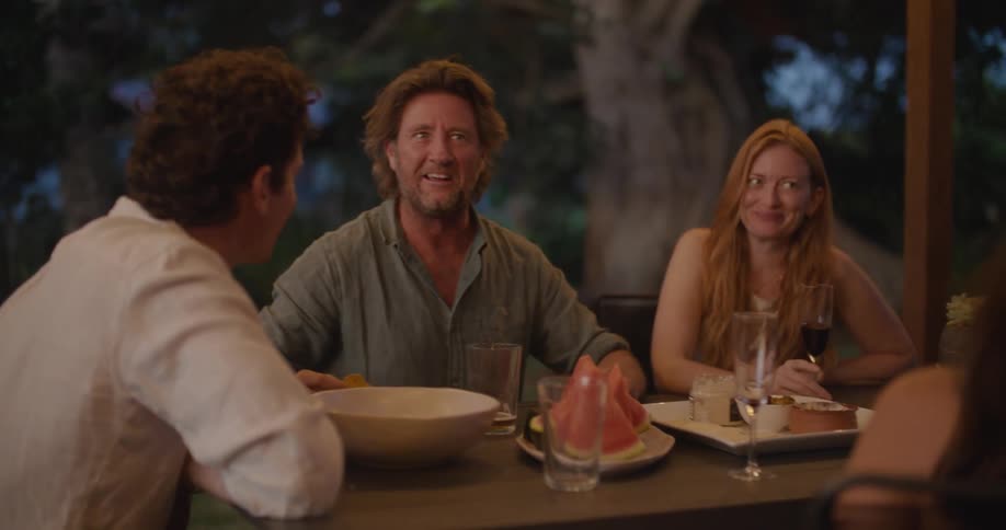 Two men and two women sit outside on a patio and eat and drink and talk and laugh together