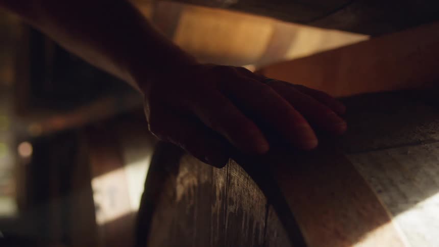 A distiller rubbing a barrel in a dimly lit cellar