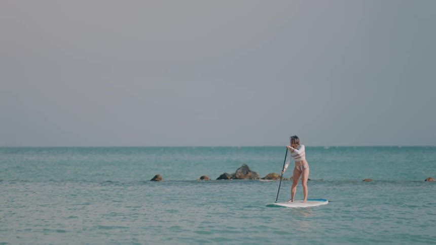 A woman is paddling on a surfboard in the ocean