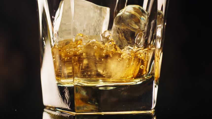 Liquid pours into a glass with ice cubes as bubbles rise to the top