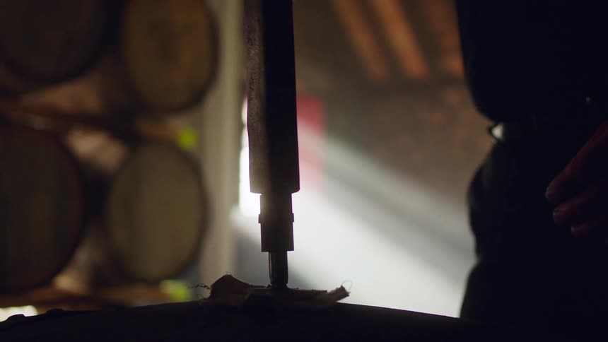 Person opens cask of liquor standing in dim room silhouetted by sun from window