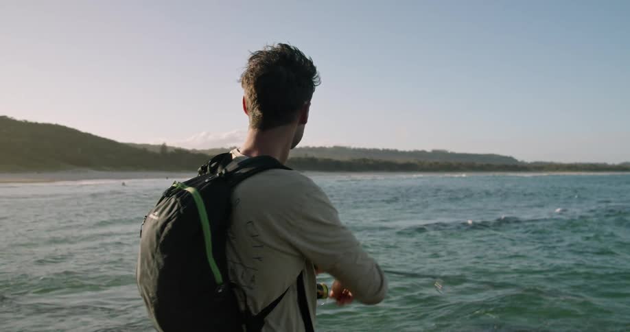 A man fishes while standing on a rocky coastline during the day
