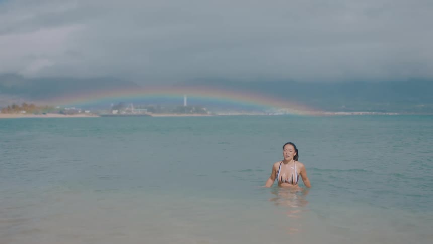 A woman is swimming in the ocean and a rainbow is in the sky in the distance