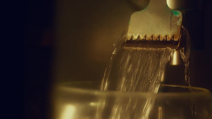 Water flowing from a flat sprout into a glass vase indoors