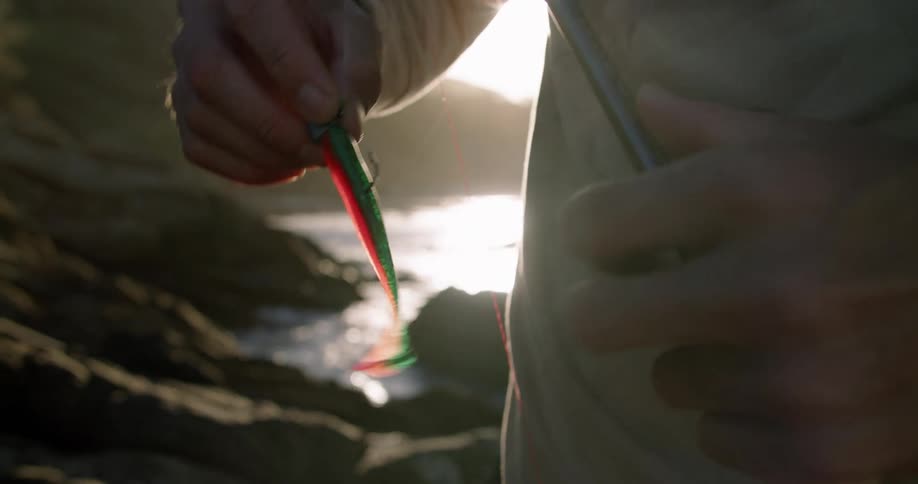 A man attaches bait to his fishing hook while standing on a rocky coastline during the day