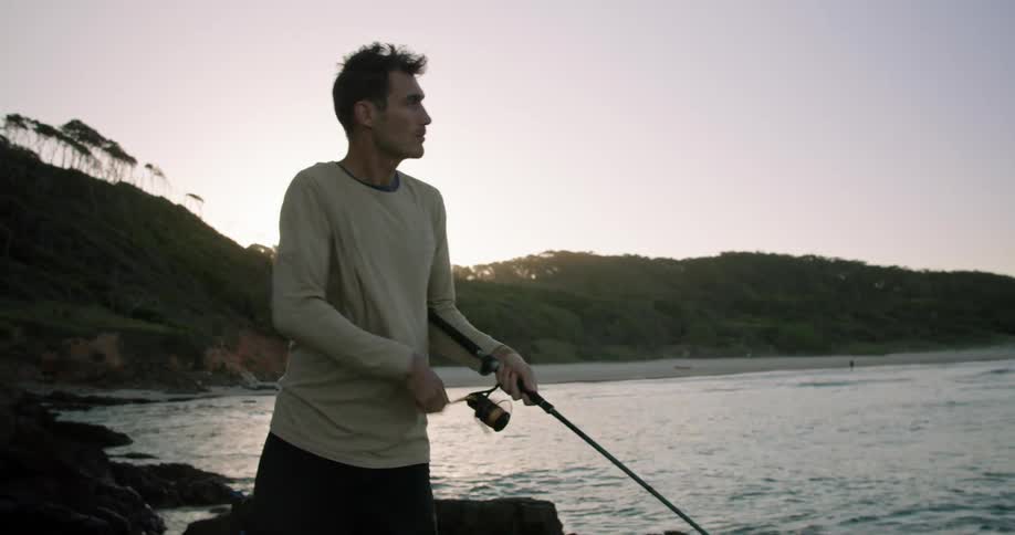 A man is standing on a rocky shore and fishing during the day