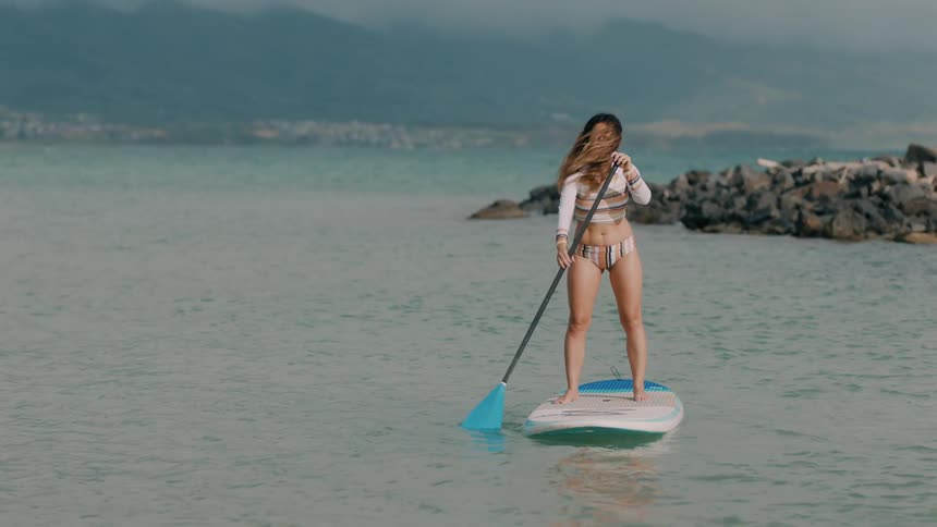 Young woman wearing sports swimwear standing over a surfboard rowing near the coast