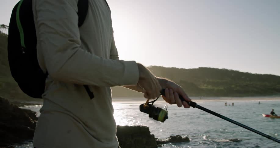 A man standing on the coast casts his fishing line into the ocean