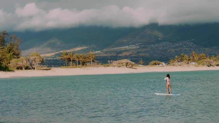 A woman is paddling on a surfboard by the shore