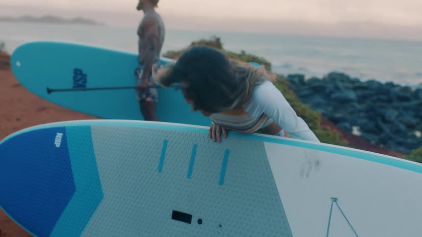 A man and woman outdoors carrying surfboards