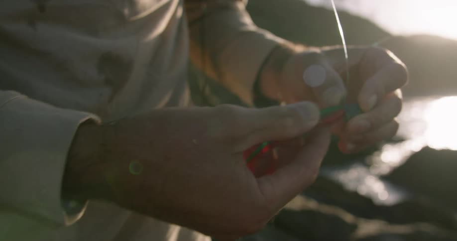 Person puts lure on to fishing hook standing on shore