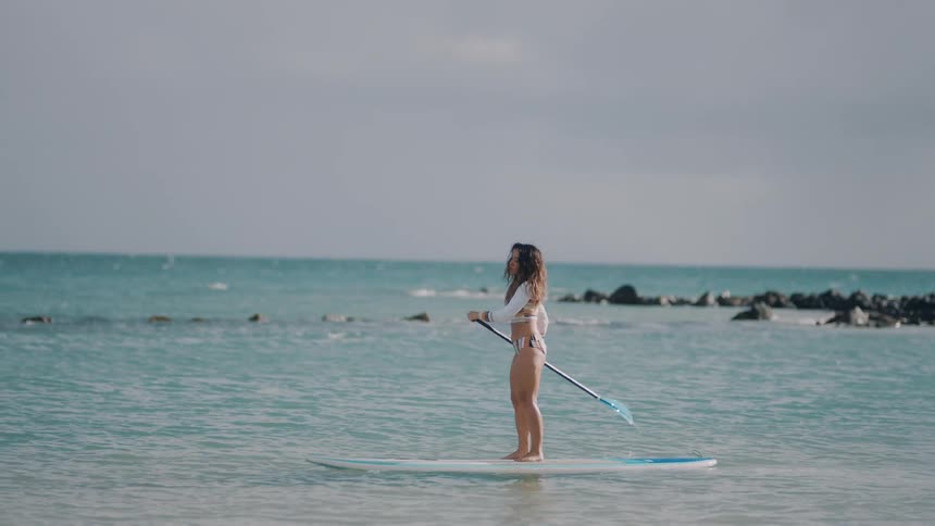 A woman paddles while standing on the surfboard